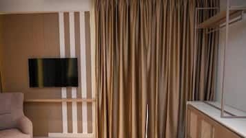 A room with a flat-screen TV mounted on a wooden panel, a beige sofa, and a curtain with a vertical striped pattern.