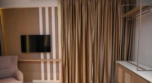 A room with a flat-screen TV mounted on a wooden panel, a beige sofa, and a curtain with a vertical striped pattern. - Skanderbeg Resort - Koral Hospitality (Golem)