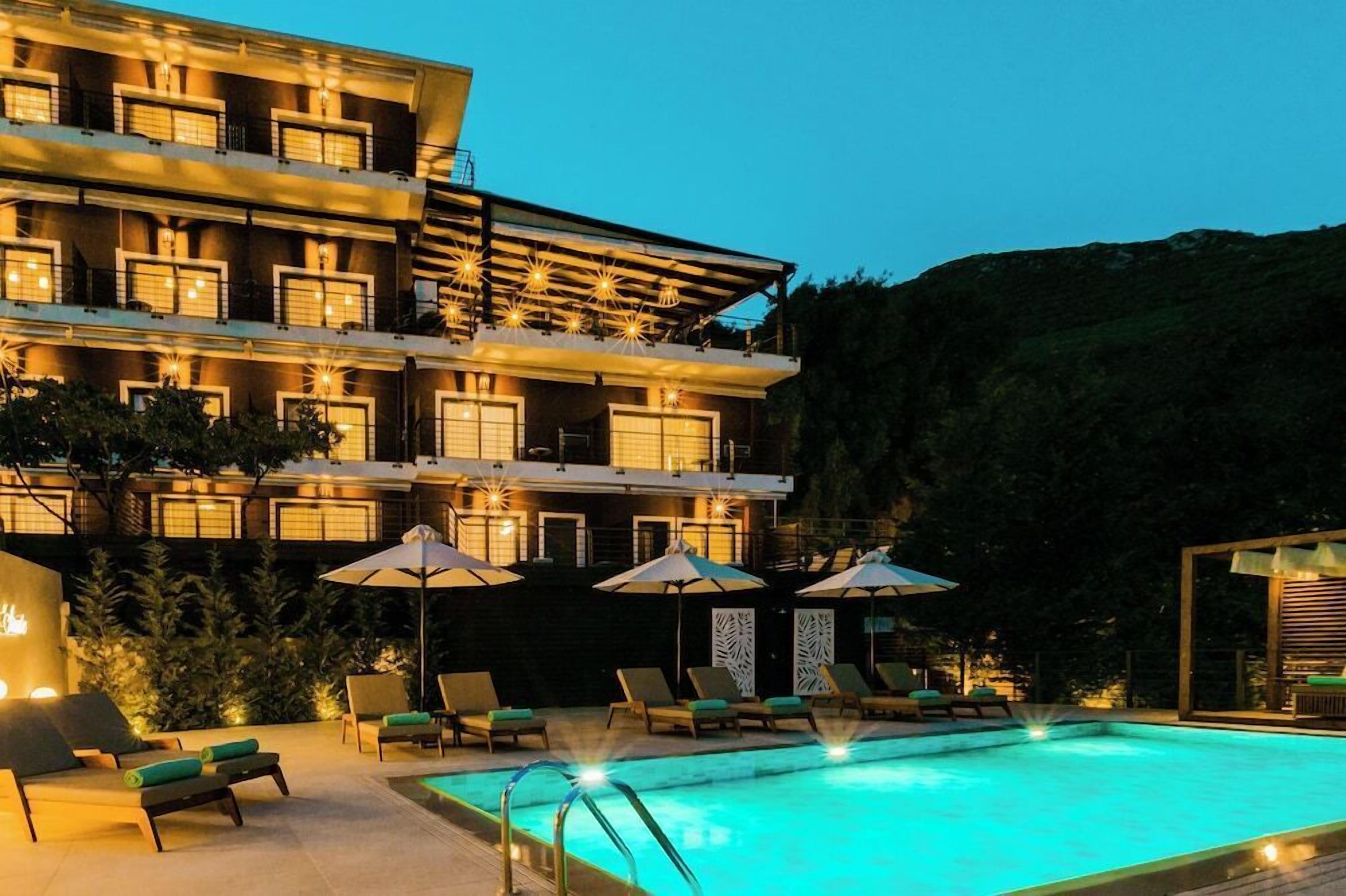 A multi-story hotel with a swimming pool, outdoor seating, and a mountainous backdrop.