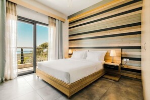 Habitación de hotel moderna con una cama grande, cabecera de madera y vistas al exterior desde un balcón.