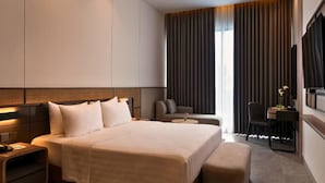 A modern hotel room with a large bed, bedside tables, a seating area with a sofa and armchairs, a desk with a chair, and a TV mounted on the wall. - Laska Hotel and Resort Ciater (Ciater)