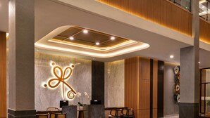 A modern lobby with a reception desk, seating area, and a decorative wall with a light fixture. - Laska Hotel and Resort Ciater (Ciater)