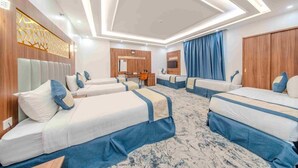 Habitación de hotel con cuatro camas alineadas, un escritorio, un espejo y un televisor.