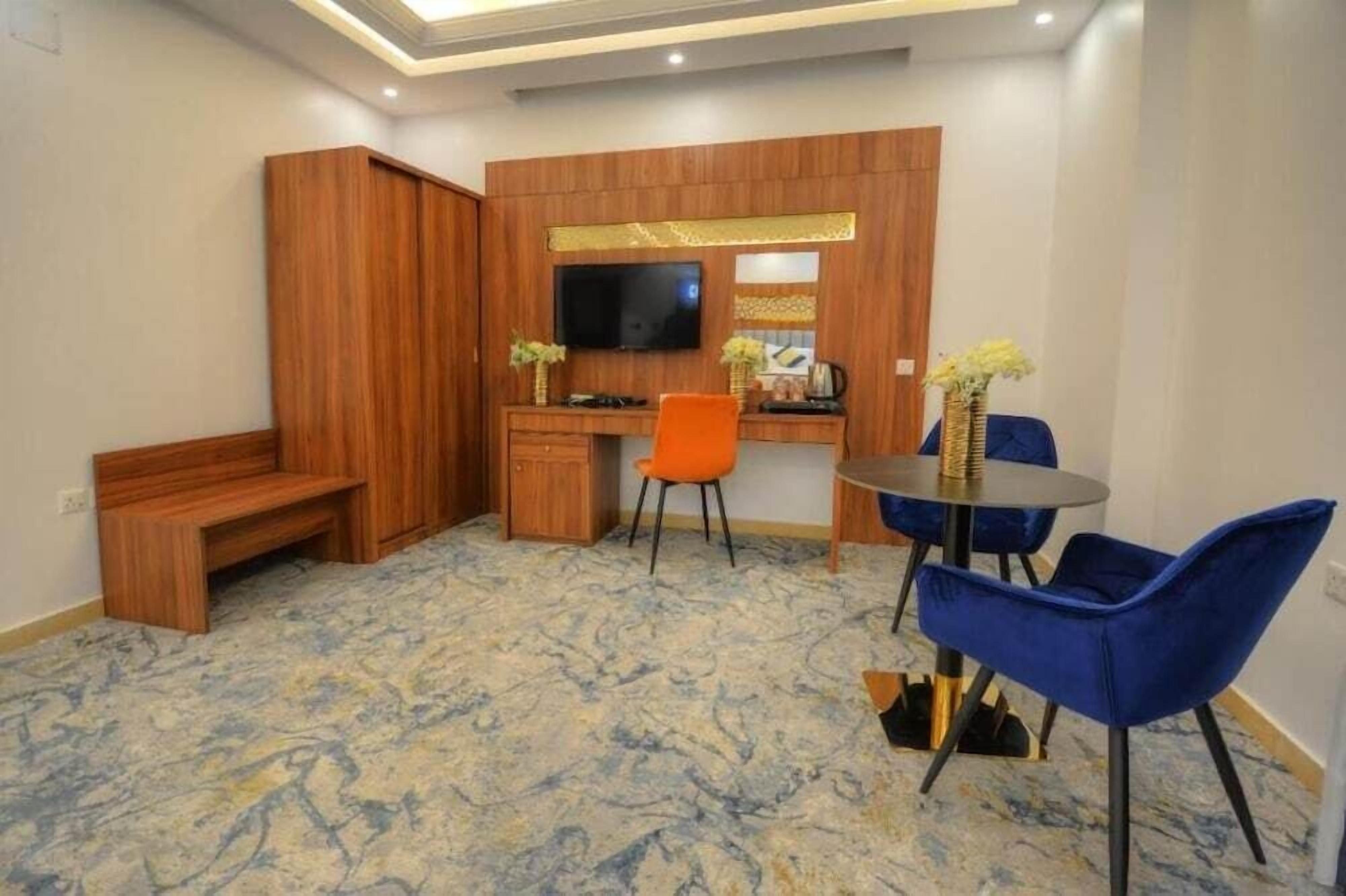Una habitación con un escritorio de madera, televisor, banca y comedor con sillas azules.