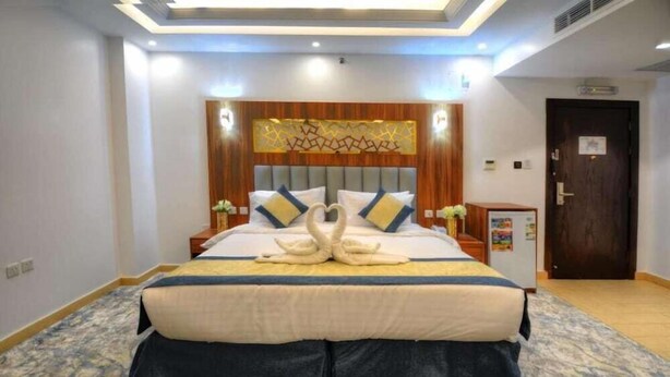 A hotel room with a large bed, a wooden headboard, and a decorative wall piece. - Almarzam Hotel (Madinah)