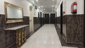 A hotel corridor with a marble floor, a reception desk with a gold-framed mirror, and a fire extinguisher on the wall. - Almarzam Hotel (Madinah)