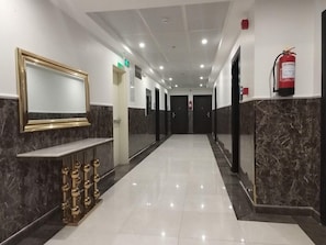 Un pasillo de hotel con suelo de mármol, una recepción con un espejo de marco dorado y un extintor en la pared.
