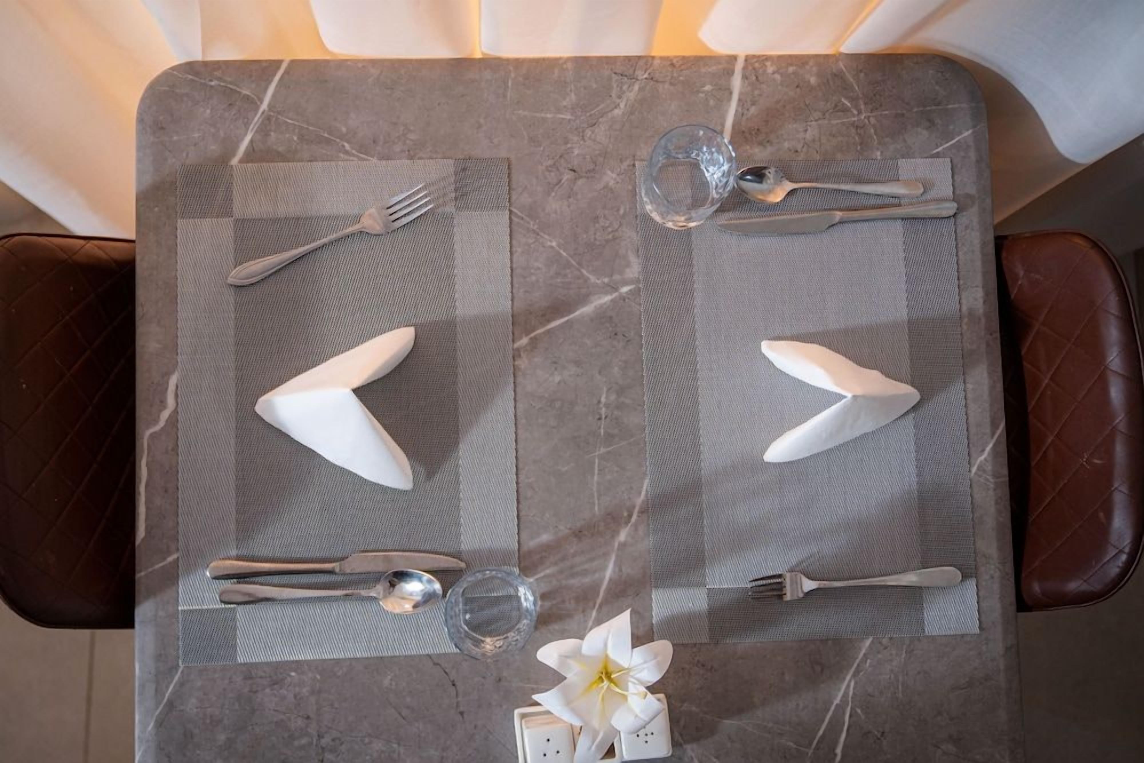 A dining table with a marble top, two chairs, and a single white flower.