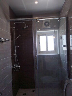 Une salle de bain moderne dotée d’une douche à parois de verre, de toilettes et d’une fenêtre laissant entrer la lumière naturelle.