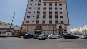 A multi-story building with a central entrance and a parking lot in front. - Almarzam Hotel (Madinah)