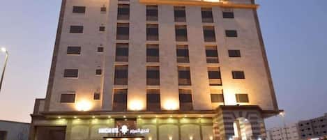 Um hotel de vários andares com fachada moderna, janelas iluminadas e entrada visível com uma placa.