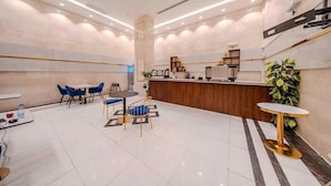 A hotel lobby with a reception desk, seating area, and a large plant. - Almarzam Hotel (Madinah)