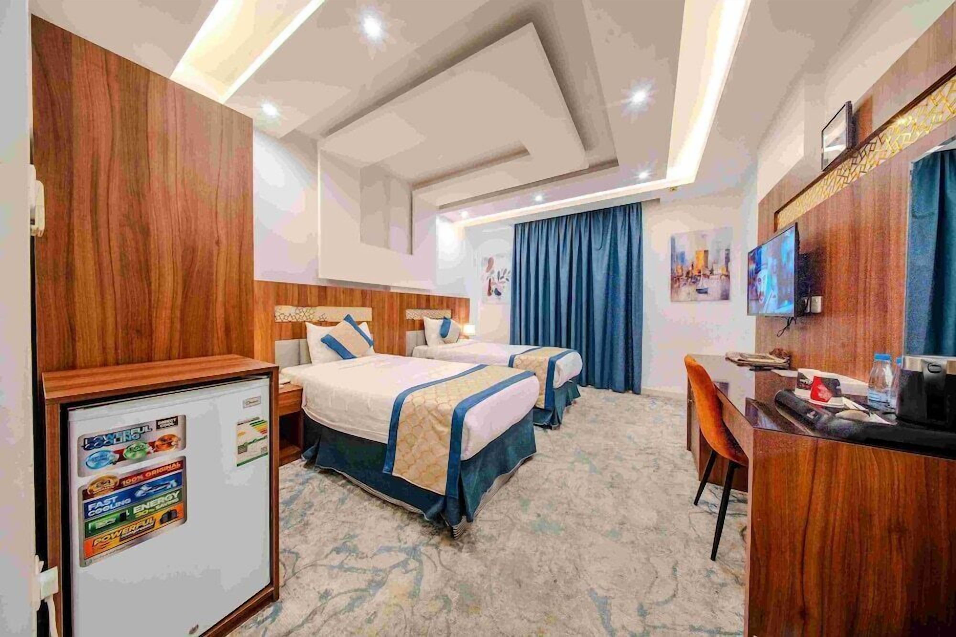 Quarto de hotel com duas camas, uma mesa, uma televisão e um frigorífico.
