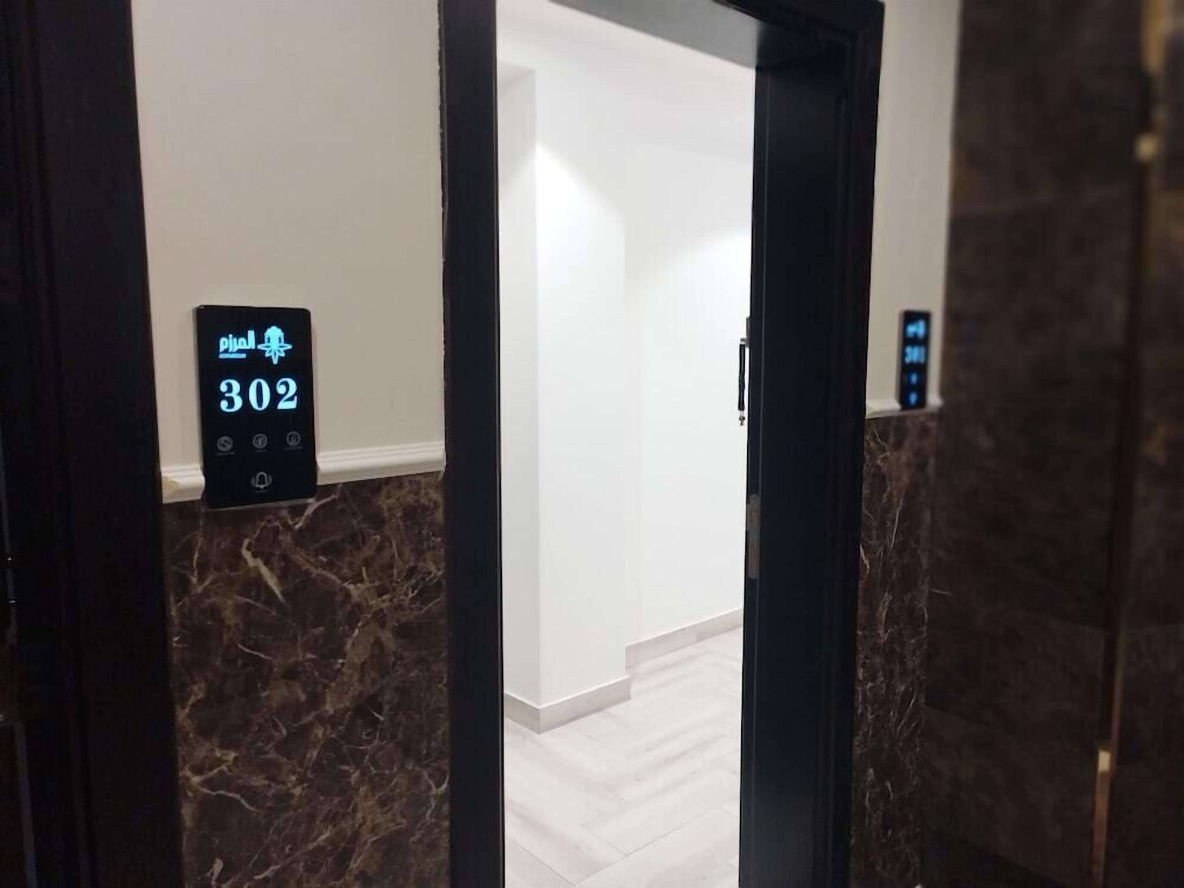 Un pasillo interior con piso de mármol, un panel de control de ascensor digital que muestra el número 302 y una pared blanca lisa.