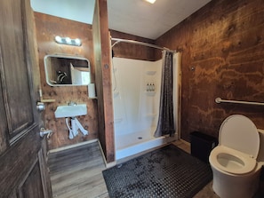 A bathroom with a wooden wall, a white sink, a mirror, a shower with a glass door, and a toilet.