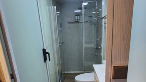 A bathroom with a glass shower enclosure, a toilet, and a sink.
