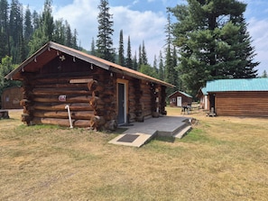 A rustic log cabin with a door, a sign indicating 'No Parking,' and a small outdoor seating area.