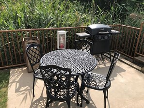 Eine Terrasse mit rundem Tisch, vier Stühlen, einem Grill und einer Mülltonne.