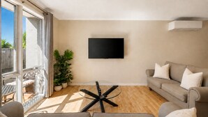 A living room with a flat-screen TV mounted on the wall, a glass coffee table, a sofa, and a potted plant. - Park Street Retreat Cowes by Ready Set Stay (Cowes)