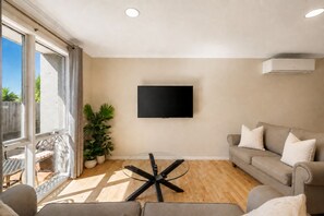 A living room with a flat-screen TV mounted on the wall, a glass coffee table, a sofa, and a potted plant. - Park Street Retreat Cowes by Ready Set Stay (Cowes)