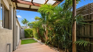 A narrow concrete pathway flanked by lush green plants and a wooden fence, leading to a building with a window and a door. - Park Street Retreat Cowes by Ready Set Stay (Cowes)