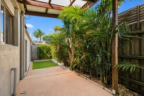 A narrow concrete pathway flanked by lush green plants and a wooden fence, leading to a building with a window and a door. - Park Street Retreat Cowes by Ready Set Stay (Cowes)