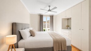 A bedroom with a bed, bedside lamp, ceiling fan, and a view of the outdoors. - Park Street Retreat Cowes by Ready Set Stay (Cowes)