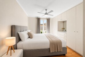 A bedroom with a bed, bedside lamp, ceiling fan, and a view of the outdoors. - Park Street Retreat Cowes by Ready Set Stay (Cowes)