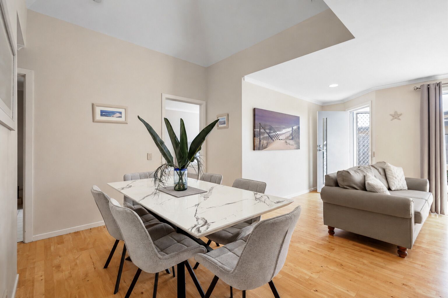 Una sala de estar moderna con un sofá gris, una mesa de comedor con seis sillas y una planta grande.