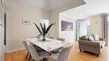 Una sala de estar moderna con un sofá gris, una mesa de comedor con seis sillas y una planta grande.