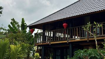 A building with a tiled roof, a wooden balcony, and surrounding greenery.