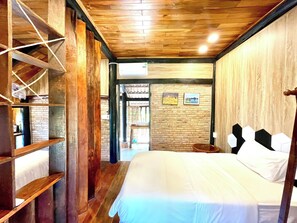 A bedroom with a wooden ceiling, a bed with white bedding, a brick wall, and two framed pictures. - Lam Mountain Retreat (Phu Quoc)