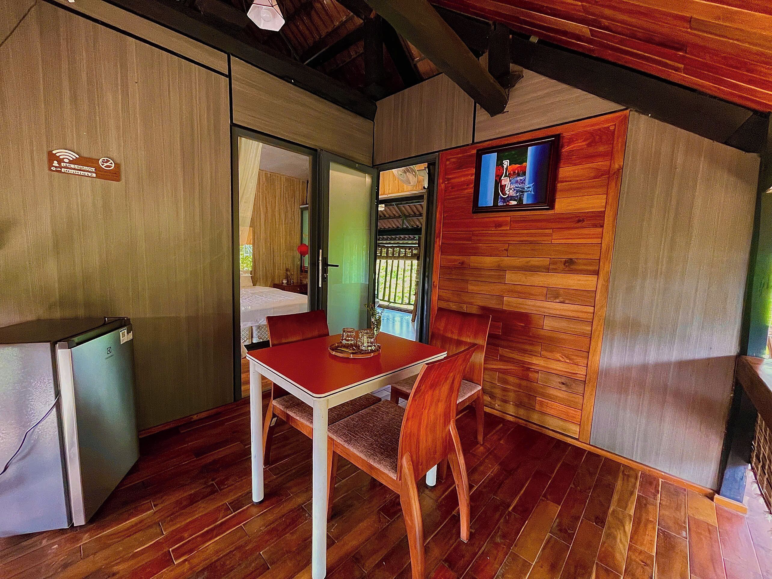 A compact room with a wooden table and chairs, a small kitchenette, and a television mounted on the wall.