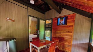 A compact room with a wooden table and chairs, a small kitchenette, and a television mounted on the wall.