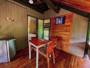 A compact room with a wooden table and chairs, a small kitchenette, and a television mounted on the wall.