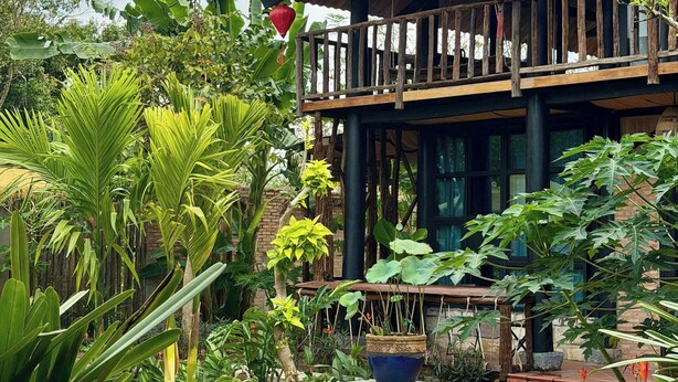A two-story building with a balcony, surrounded by lush greenery and a stone-paved courtyard.
