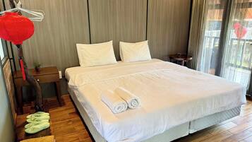 Hotellihuone, jossa on suuri sänky, kaksi tyynyä, yöpöytä, puulattia ja ikkuna, jossa on verhot.