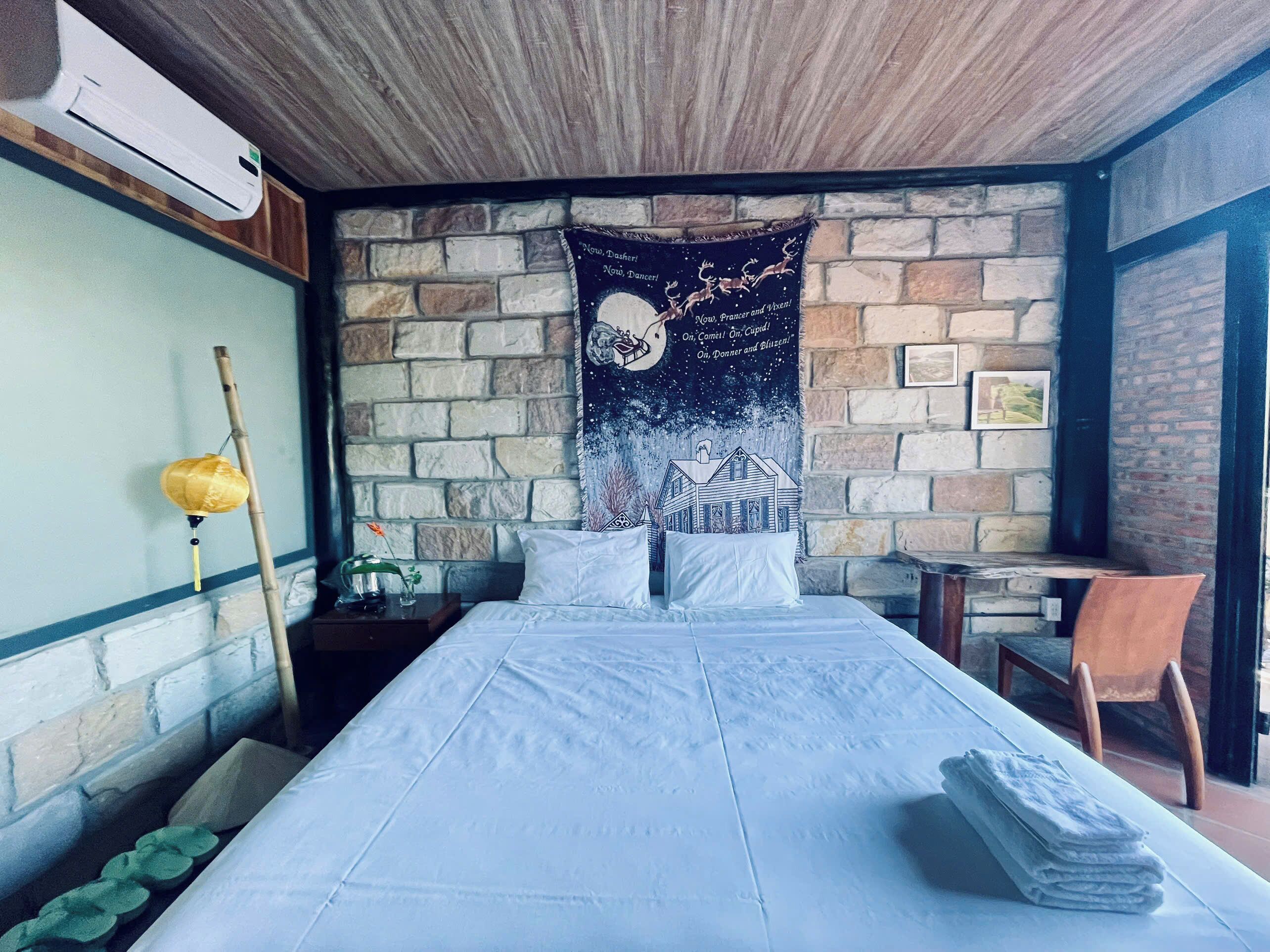 A bedroom with a bed, a nightstand, a chair, a table, a tapestry, and a window.