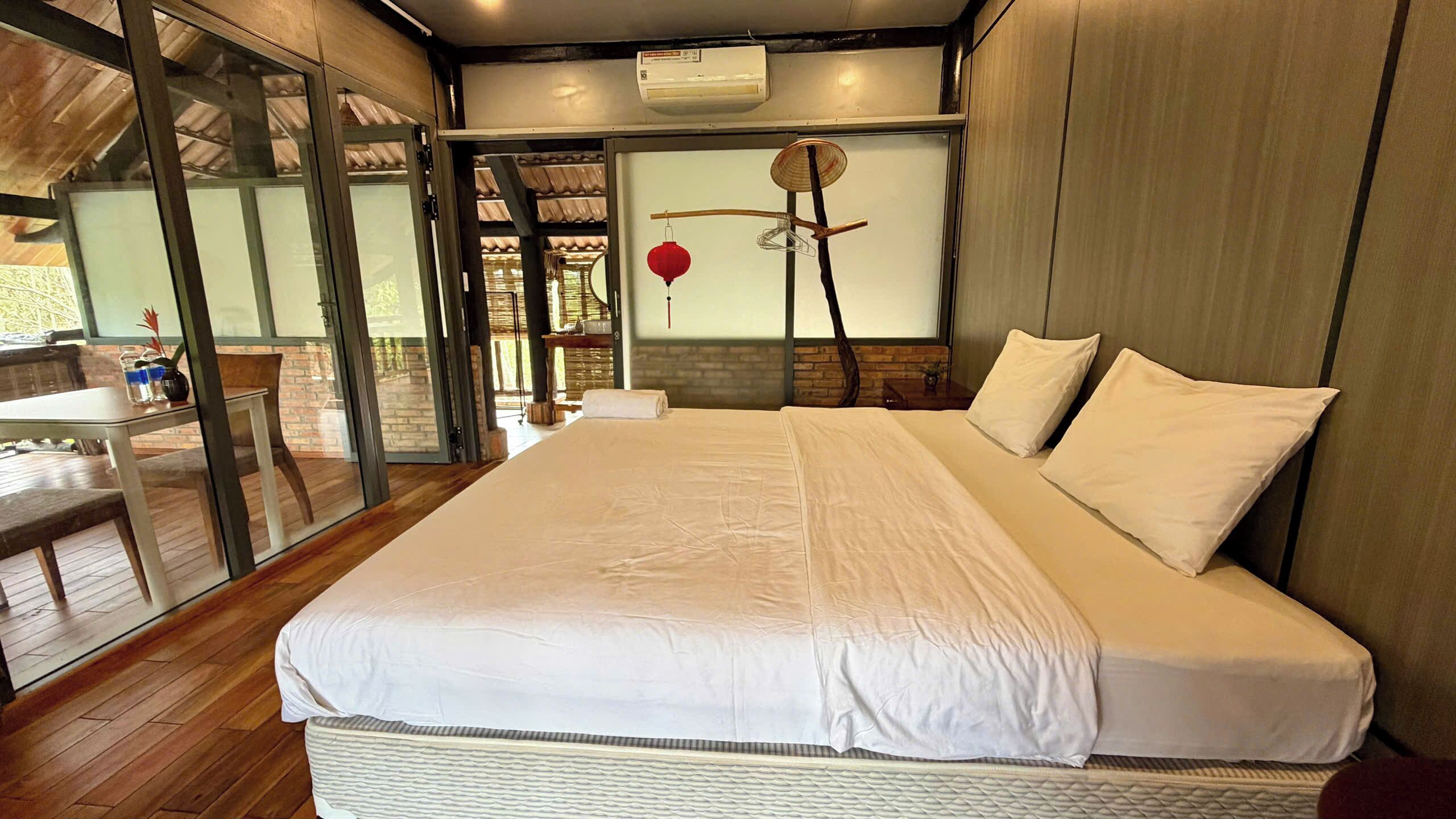 Un dormitorio con una cama grande, un ventanal de vidrio que da a un espacio exterior y un farol rojo en la pared.