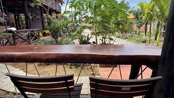 An outdoor seating area with two wooden chairs and a bench, surrounded by potted plants and a building with a balcony.