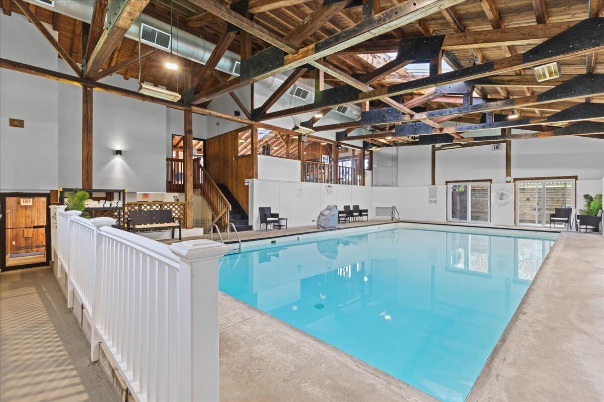 An indoor swimming pool with a wooden ceiling and a white poolside area.