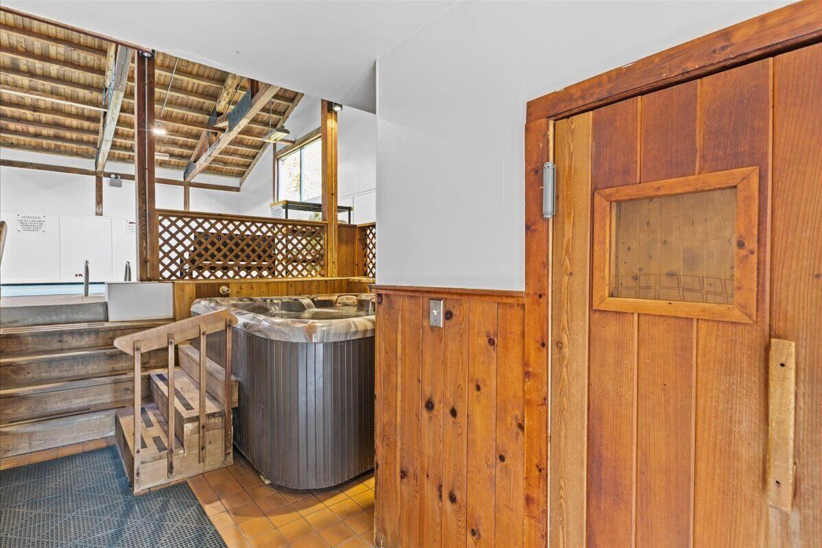 A wooden door with a metal handle, a hot tub, and a wooden staircase leading to a balcony.