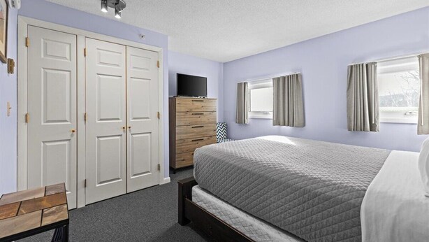 A bedroom with a bed, a dresser, a TV, and a wardrobe. - Mountain Haven | Cozy Stowe Escape (Stowe)