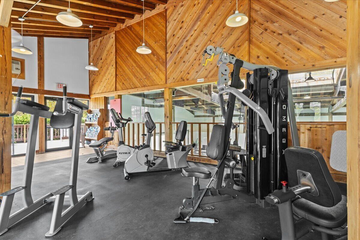 A gym with various exercise equipment, wooden ceiling, and large windows.