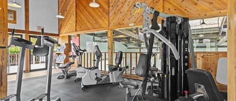 A gym with various exercise equipment, wooden ceiling, and large windows.