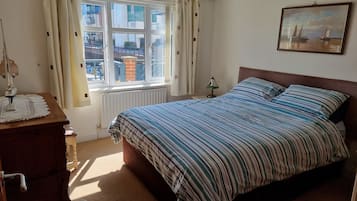 A bedroom with a bed, a dresser, a window with curtains, a radiator, and a painting on the wall.