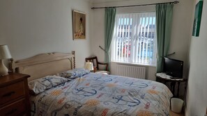A bedroom with a bed, a chair, a table with a television, a window with curtains, and a radiator. - Waterfront Marina Apartment (Exmouth)