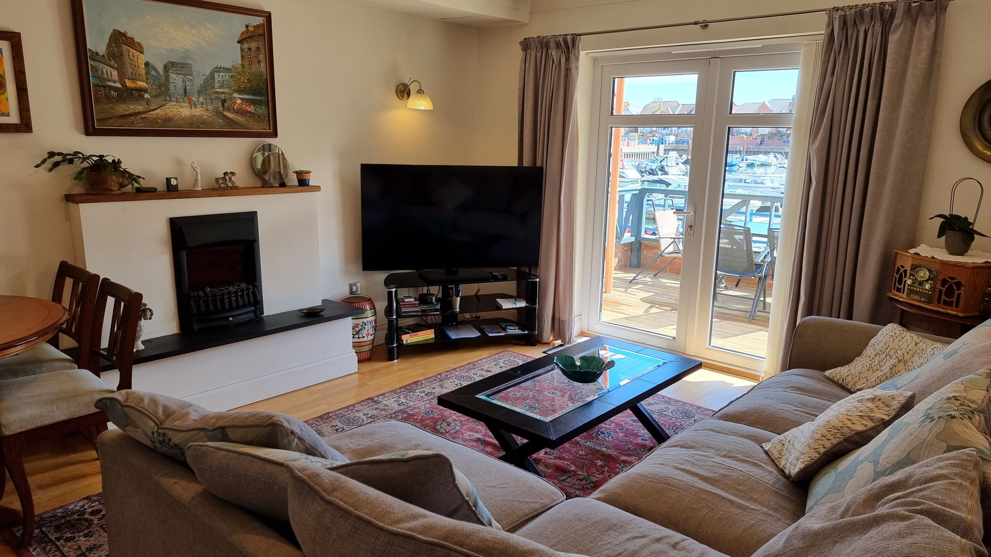 Una sala de estar con sofá, una mesa de centro, chimenea, televisor y vista a un puerto deportivo a través de puertas corredizas de vidrio.