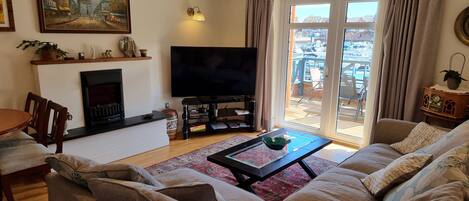 Una sala de estar con sofá, una mesa de centro, chimenea, televisor y vista a un puerto deportivo a través de puertas corredizas de vidrio.