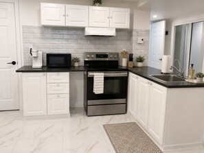 A modern kitchen with white cabinets, a black countertop, a stainless steel oven, and a microwave.